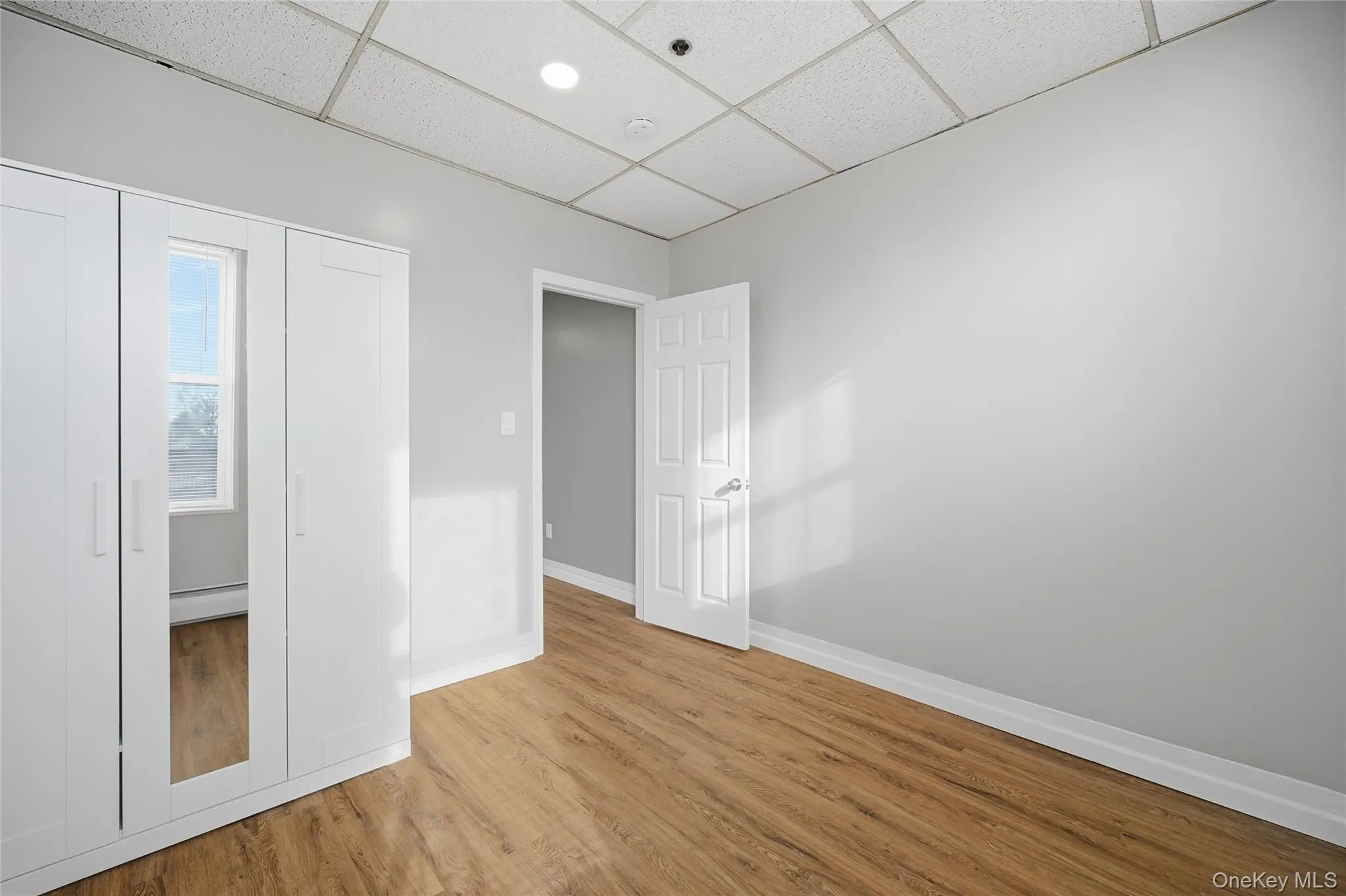 Unfurnished bedroom featuring a drop ceiling, a closet, light wood finished floors, and a baseboard heating unit Unfurnished bedroom featuring a drop ceiling, a closet, light wood finished floors, and a baseboard heating unit
