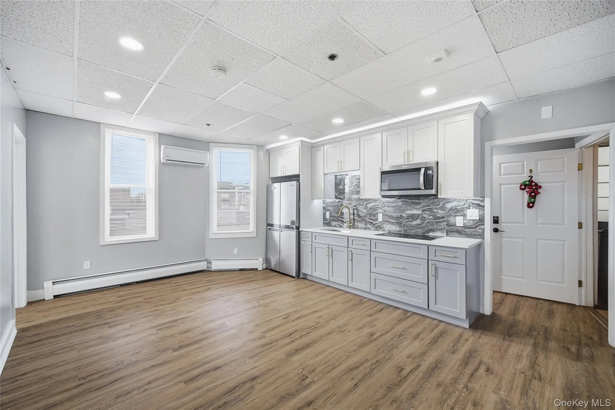 Kitchen with a paneled ceiling, light countertops, a baseboard radiator, dark wood finished floors, and stainless steel appliances Kitchen with a paneled ceiling, light countertops, a baseboard radiator, dark wood finished floors, and stainless steel appliances