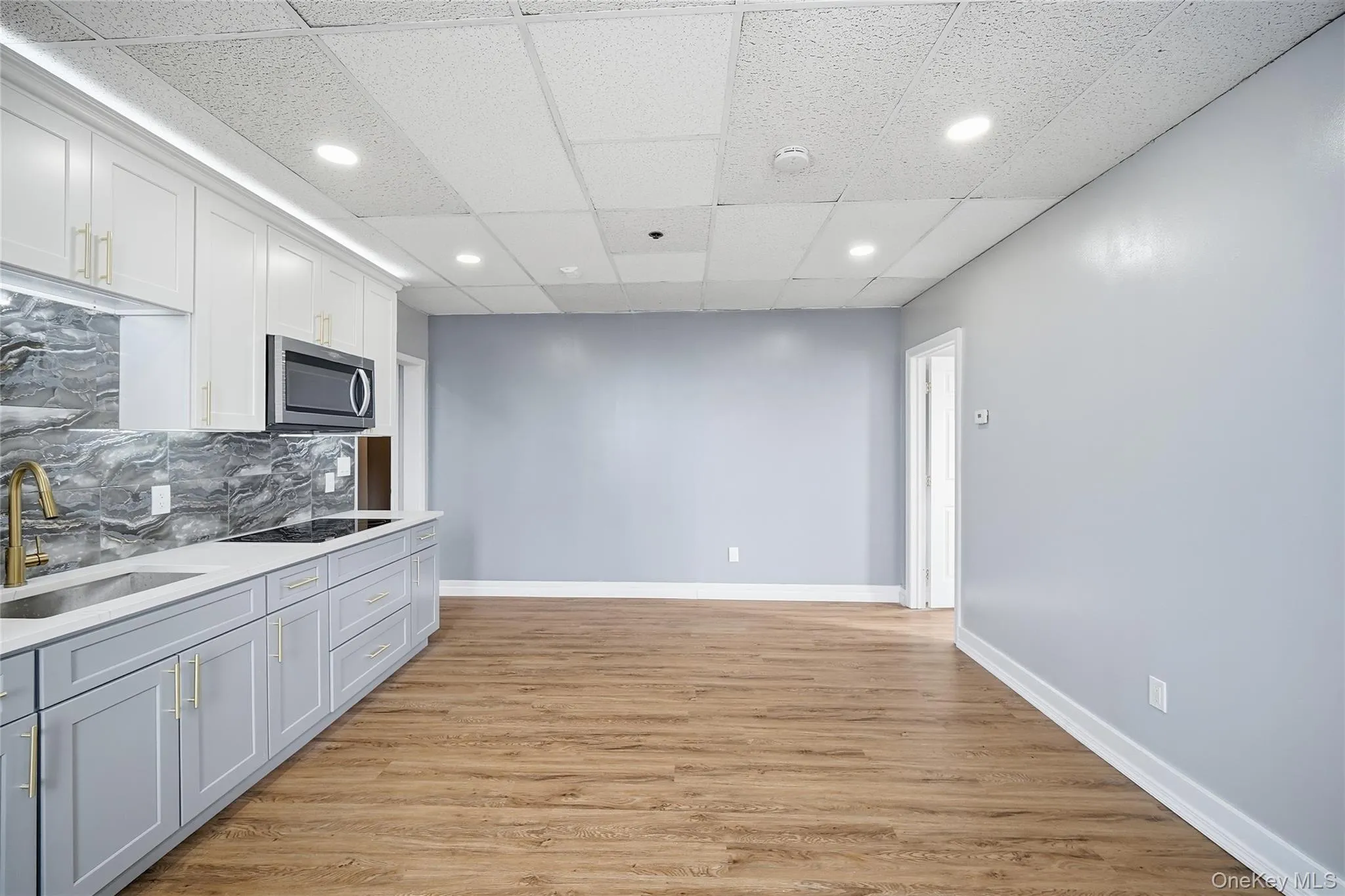 Kitchen with backsplash, recessed lighting, light wood-style flooring, a paneled ceiling, and white cabinetry Kitchen with backsplash, recessed lighting, light wood-style flooring, a paneled ceiling, and white cabinetry