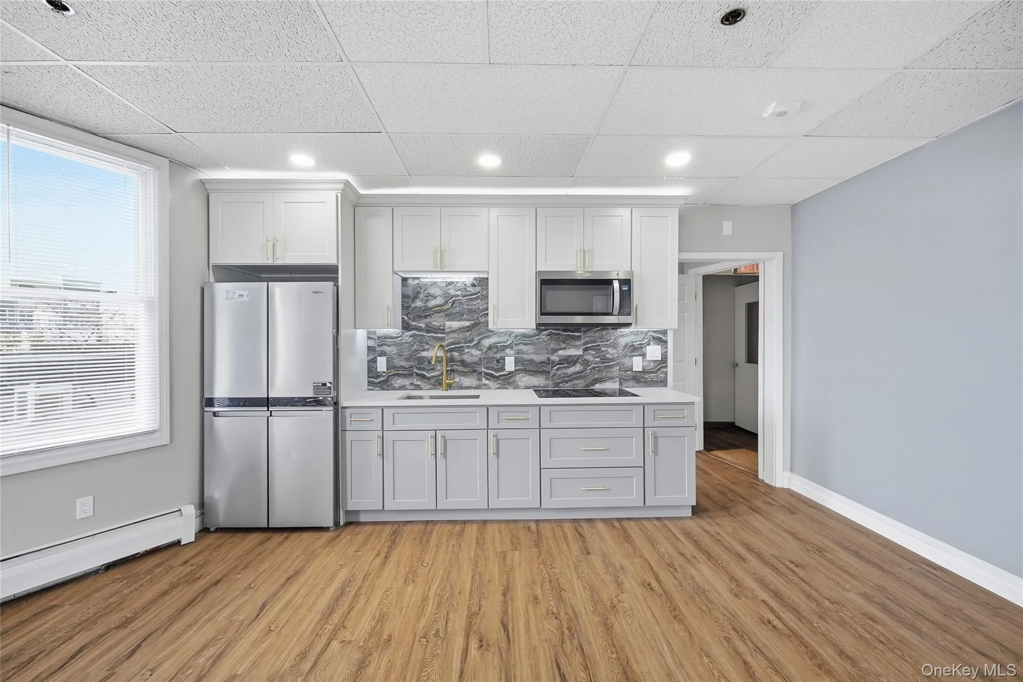 Kitchen with stainless steel appliances, decorative backsplash, light wood finished floors, a paneled ceiling, and white cabinets Kitchen with stainless steel appliances, decorative backsplash, light wood finished floors, a paneled ceiling, and white cabinets