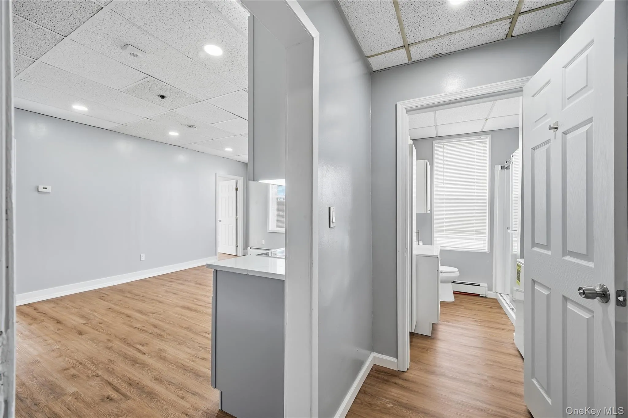 Corridor featuring a paneled ceiling, light wood-style floors, a baseboard heating unit, and recessed lighting Corridor featuring a paneled ceiling, light wood-style floors, a baseboard heating unit, and recessed lighting