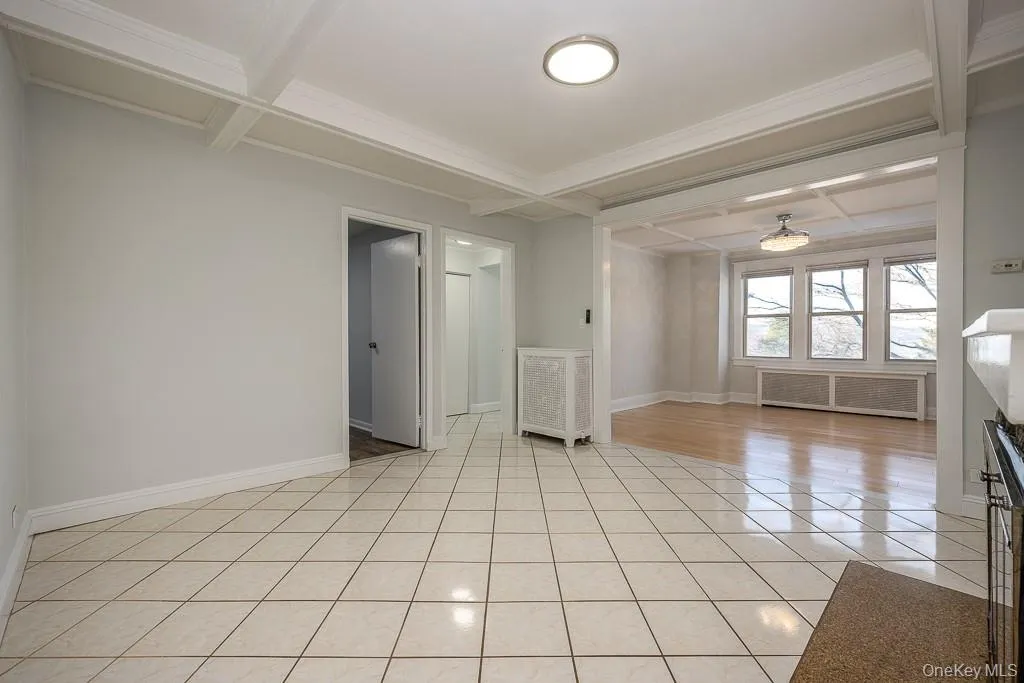 Spare room with coffered ceiling, beam ceiling, radiator, light tile patterned floors, and crown molding Spare room with coffered ceiling, beam ceiling, radiator, light tile patterned floors, and crown molding
