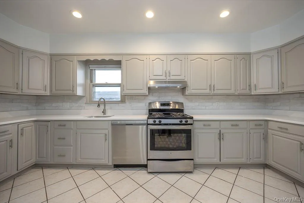 Kitchen featuring appliances with stainless steel finishes, under cabinet range hood, decorative backsplash, recessed lighting, and light tile patterned flooring Kitchen featuring appliances with stainless steel finishes, under cabinet range hood, decorative backsplash, recessed lighting, and light tile patterned flooring