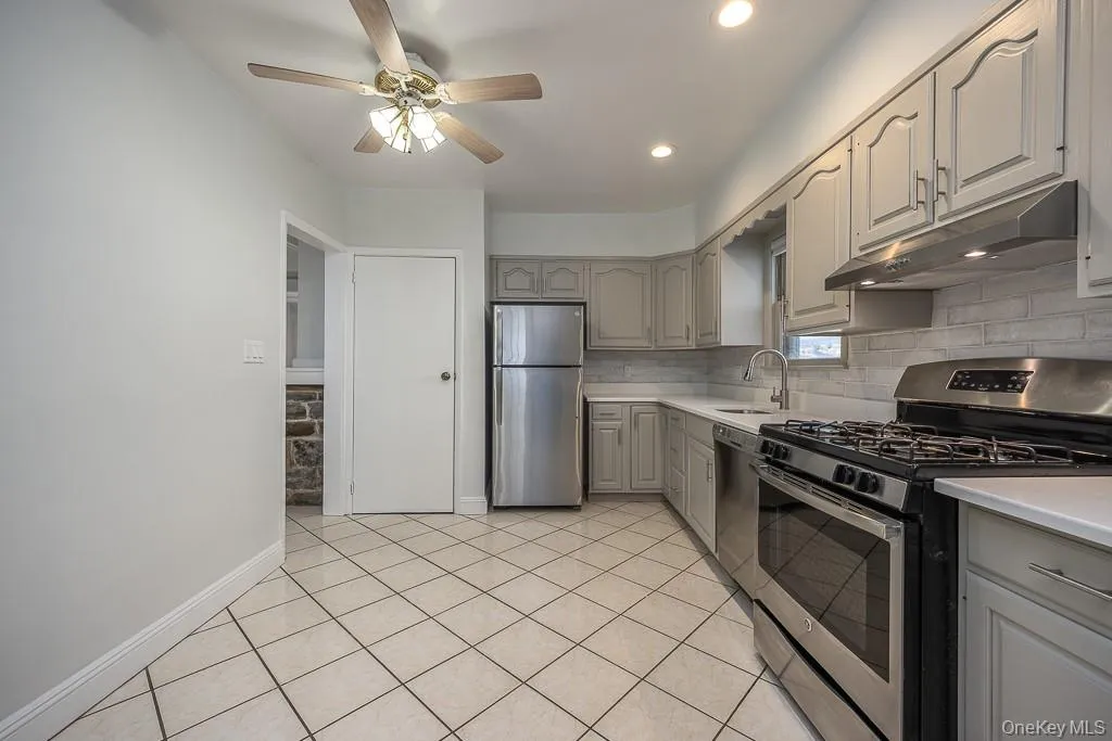 Kitchen featuring stainless steel appliances, gray cabinetry, under cabinet range hood, light countertops, and a ceiling fan Kitchen featuring stainless steel appliances, gray cabinetry, under cabinet range hood, light countertops, and a ceiling fan