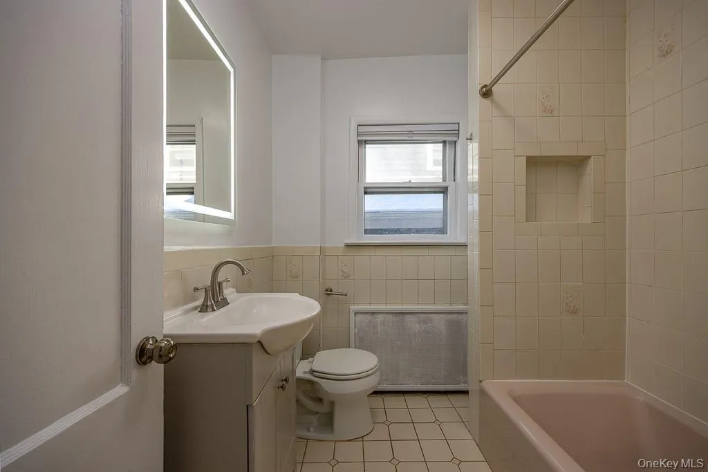Full bath with vanity, tile walls, bathtub / shower combination, a wainscoted wall, and light tile patterned floors Full bath with vanity, tile walls, bathtub / shower combination, a wainscoted wall, and light tile patterned floors