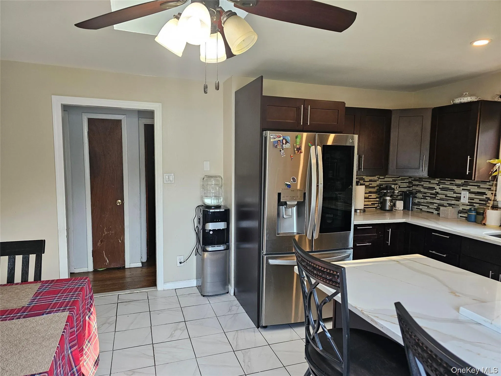 Kitchen with stainless steel fridge with ice dispenser, light stone countertops, a ceiling fan, backsplash, and dark brown cabinets Kitchen with stainless steel fridge with ice dispenser, light stone countertops, a ceiling fan, backsplash, and dark brown cabinets