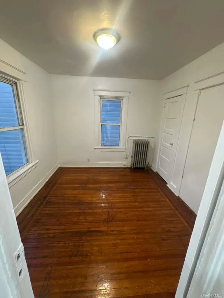 Unfurnished bedroom with dark wood-style floors and radiator heating unit Unfurnished bedroom with dark wood-style floors and radiator heating unit