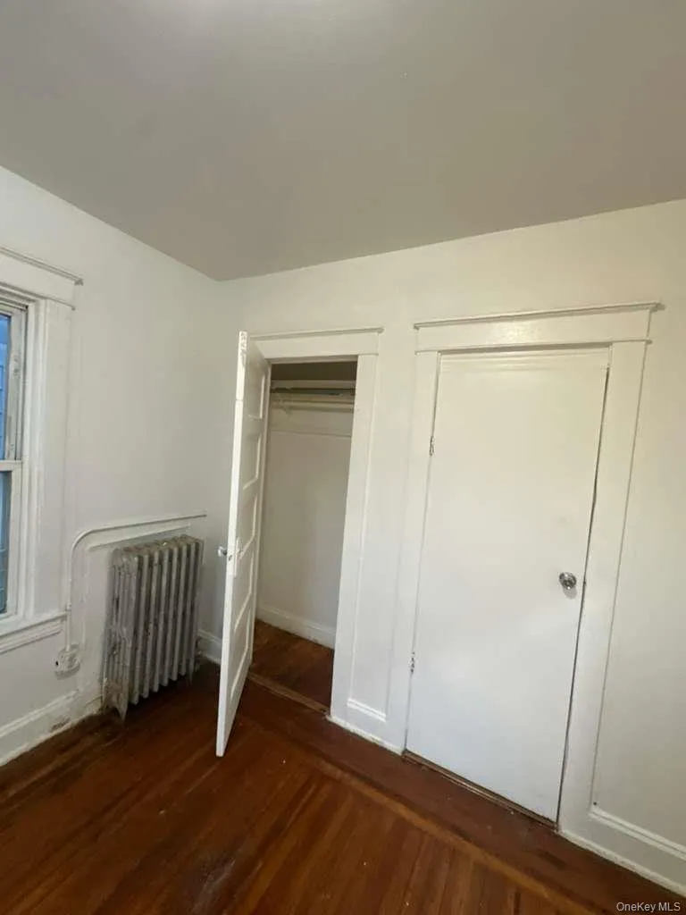 Unfurnished bedroom featuring dark wood-style floors, radiator heating unit, and a closet Unfurnished bedroom featuring dark wood-style floors, radiator heating unit, and a closet