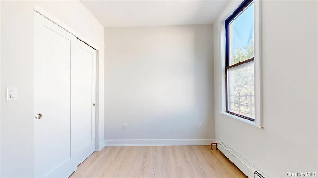 Unfurnished bedroom featuring a baseboard radiator, a closet, and light wood-style floors Unfurnished bedroom featuring a baseboard radiator, a closet, and light wood-style floors