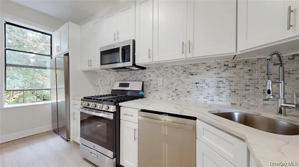 Kitchen featuring appliances with stainless steel finishes, white cabinetry, light stone counters, and decorative backsplash Kitchen featuring appliances with stainless steel finishes, white cabinetry, light stone counters, and decorative backsplash