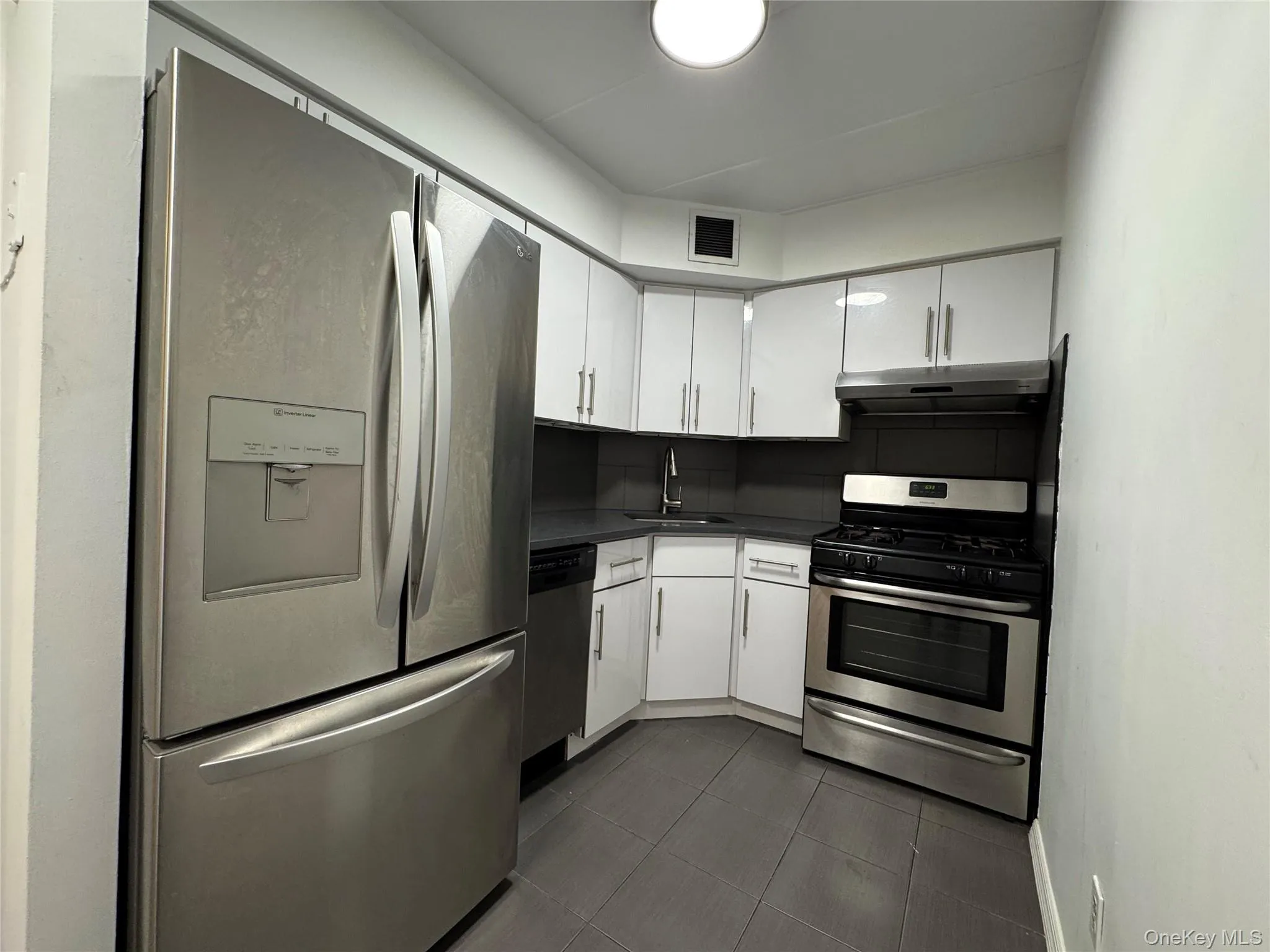 Kitchen featuring stainless steel appliances, white cabinetry, dark countertops, under cabinet range hood, and dark tile patterned floors Kitchen featuring stainless steel appliances, white cabinetry, dark countertops, under cabinet range hood, and dark tile patterned floors