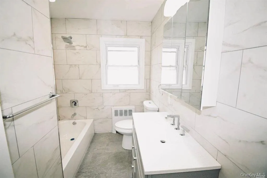 Bathroom with vanity, tile walls, shower / bath combination, and radiator heating unit Bathroom with vanity, tile walls, shower / bath combination, and radiator heating unit