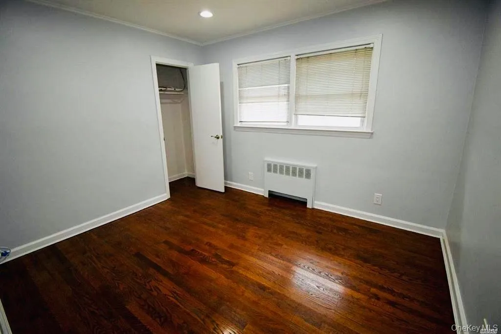 Unfurnished bedroom with radiator heating unit, dark wood finished floors, a closet, recessed lighting, and ornamental molding Unfurnished bedroom with radiator heating unit, dark wood finished floors, a closet, recessed lighting, and ornamental molding