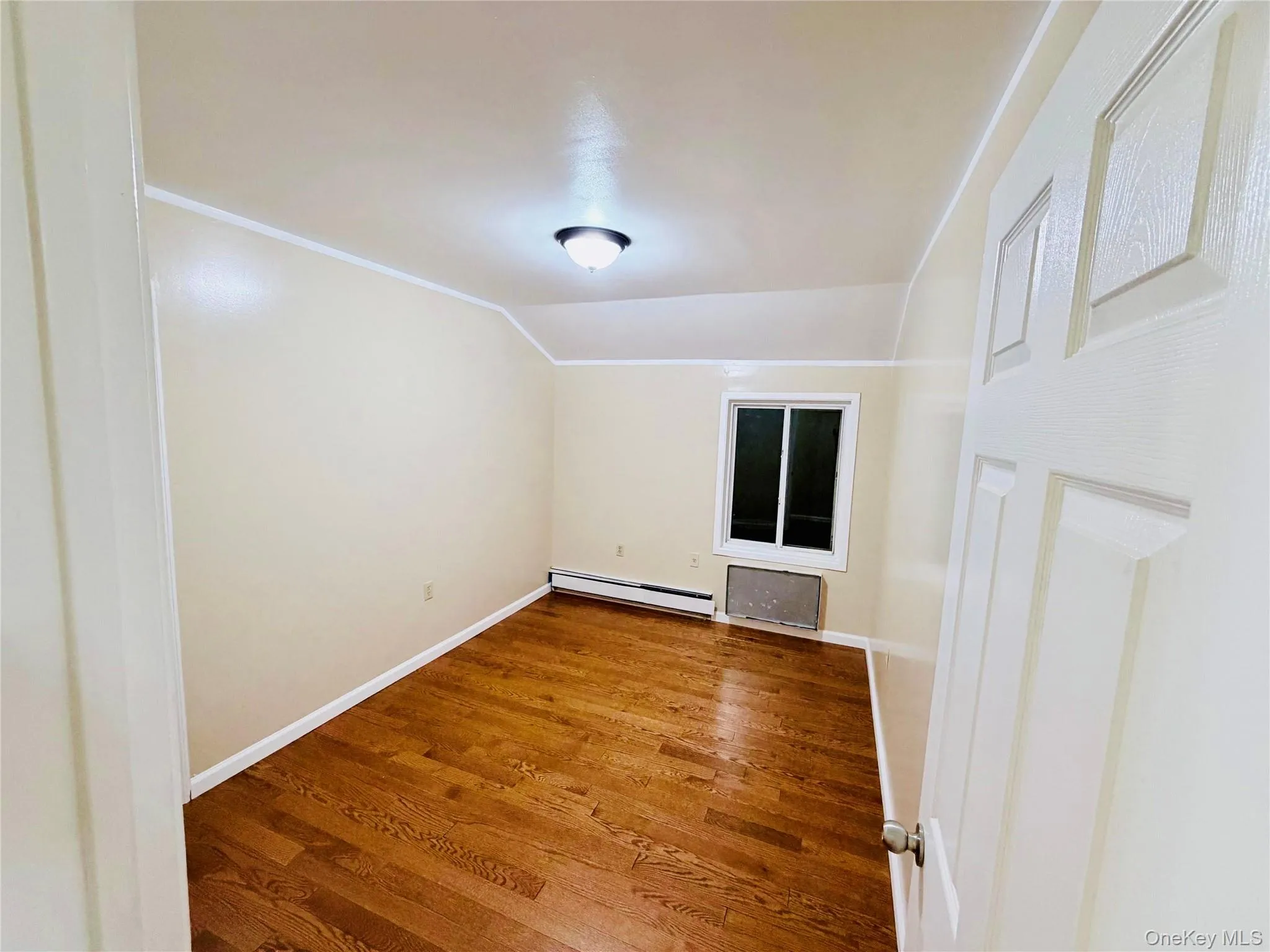 Empty room featuring wood finished floors, a baseboard radiator, crown molding, and vaulted ceiling Empty room featuring wood finished floors, a baseboard radiator, crown molding, and vaulted ceiling