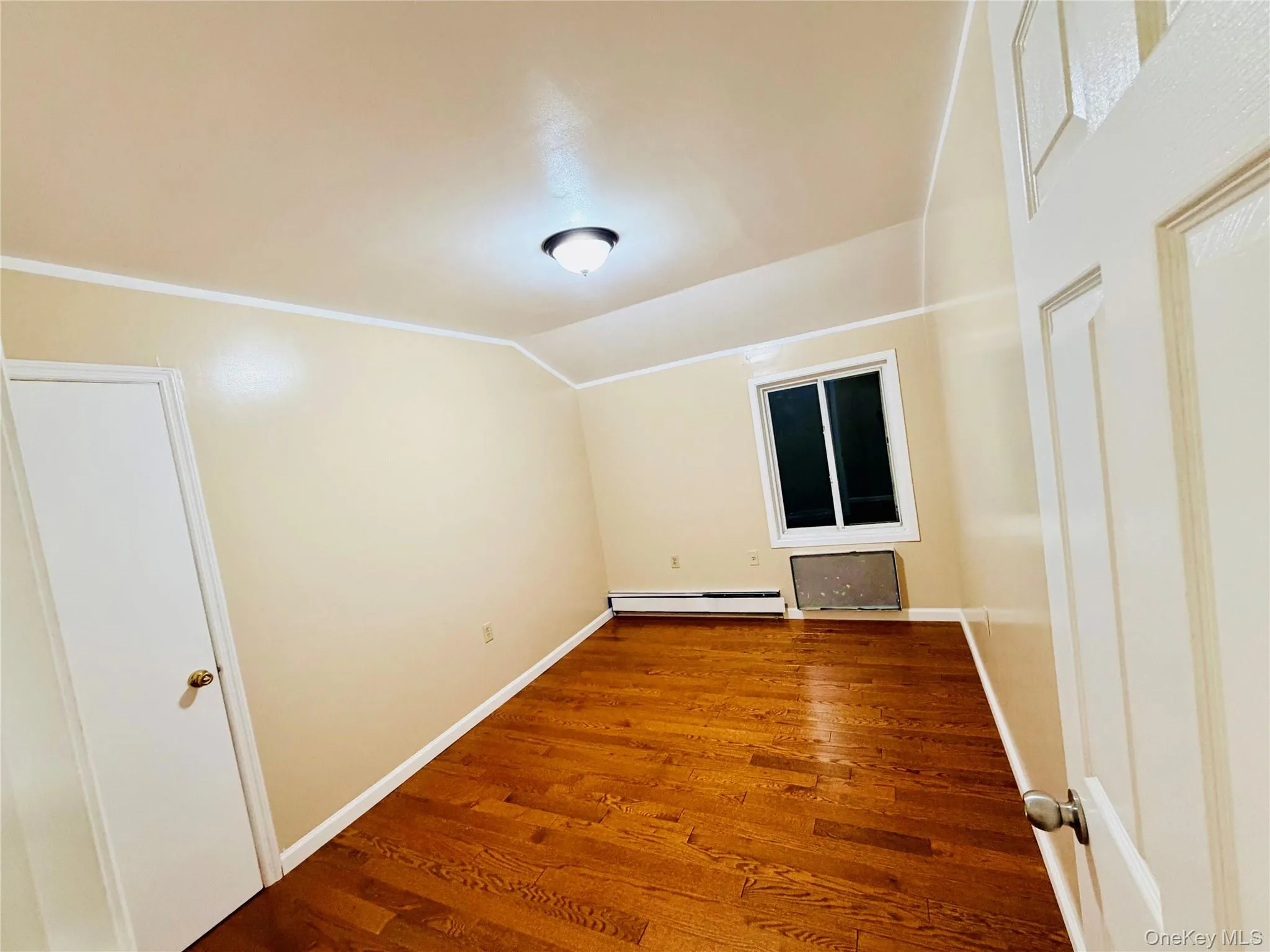 Unfurnished room featuring wood finished floors, a baseboard radiator, and vaulted ceiling Unfurnished room featuring wood finished floors, a baseboard radiator, and vaulted ceiling