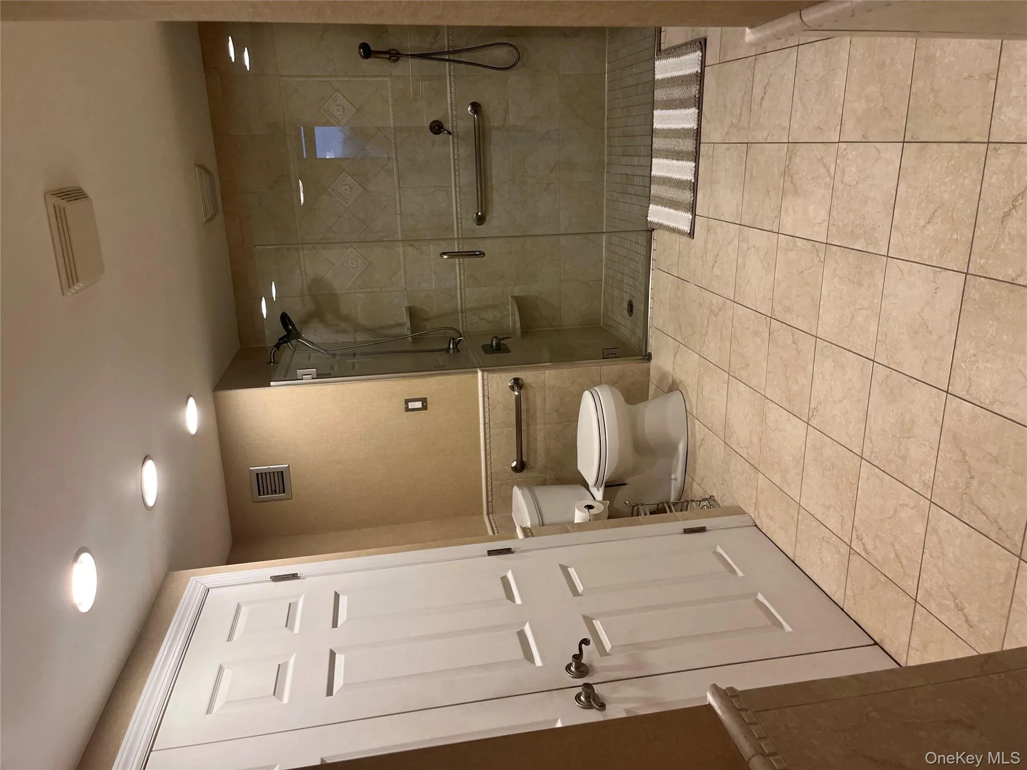 Bathroom with a shower stall, tile walls, light tile patterned floors, wainscoting, and recessed lighting Bathroom with a shower stall, tile walls, light tile patterned floors, wainscoting, and recessed lighting