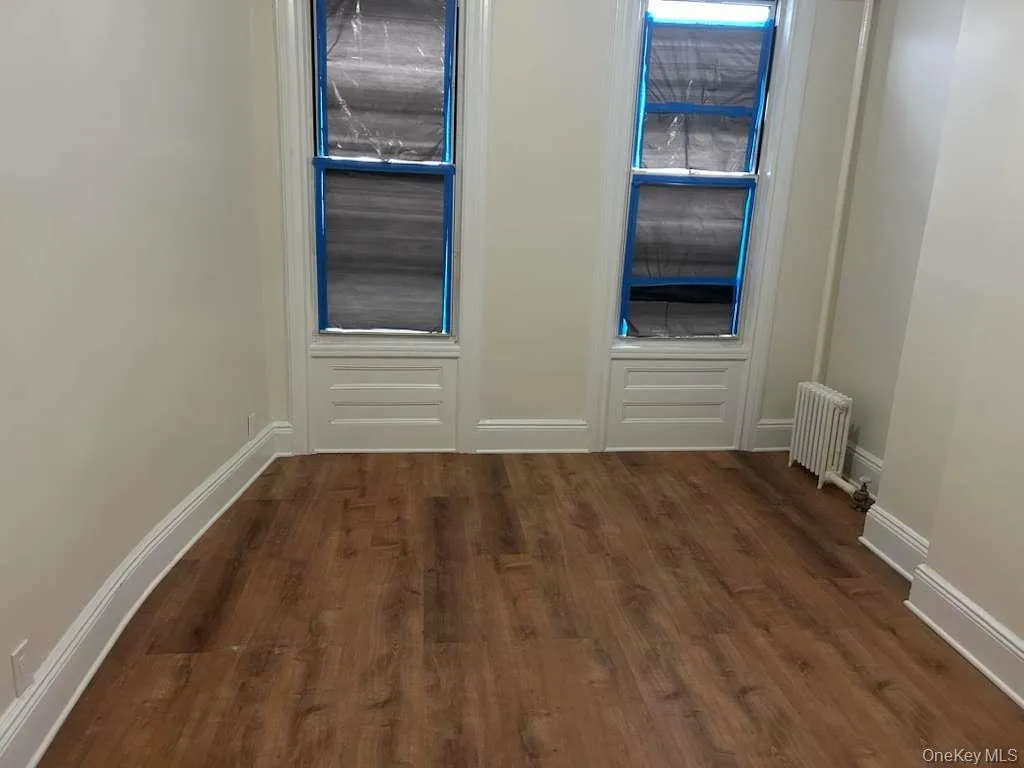 Unfurnished room featuring radiator heating unit and dark wood-type flooring Unfurnished room featuring radiator heating unit and dark wood-type flooring