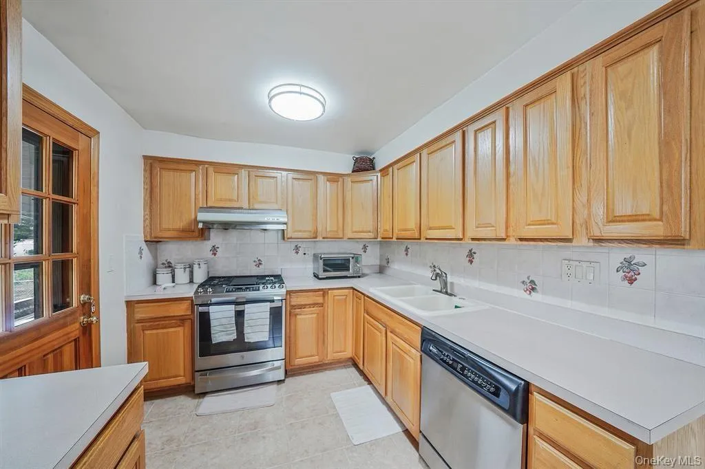Kitchen featuring appliances with stainless steel finishes, light countertops, backsplash, under cabinet range hood, and light tile patterned floors Kitchen featuring appliances with stainless steel finishes, light countertops, backsplash, under cabinet range hood, and light tile patterned floors