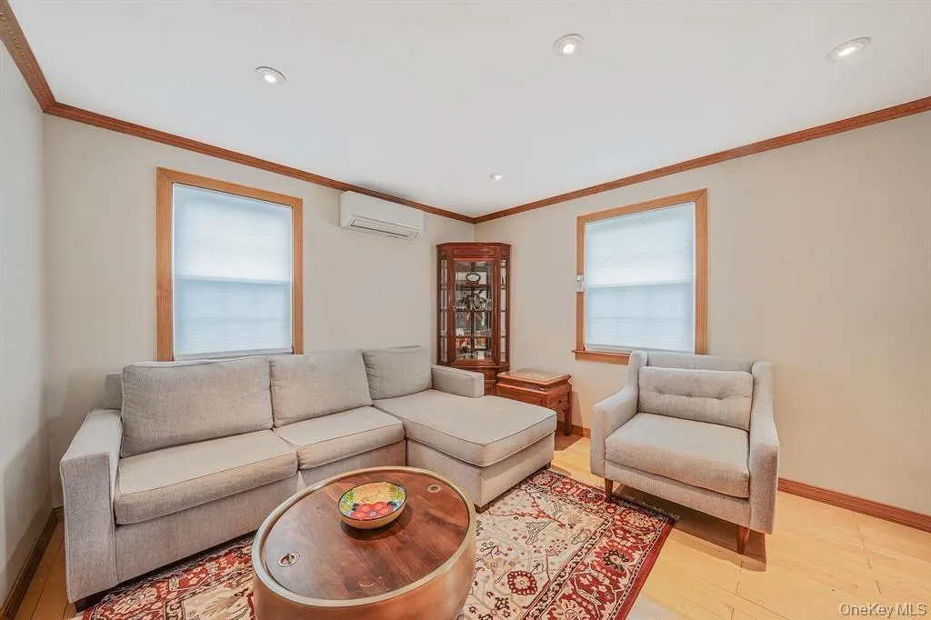 Living room featuring wood finished floors, a wall unit AC, ornamental molding, and recessed lighting Living room featuring wood finished floors, a wall unit AC, ornamental molding, and recessed lighting