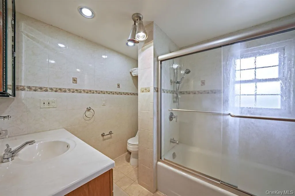 Bathroom with vanity, combined bath / shower with glass door, tile walls, recessed lighting, and light tile patterned flooring Bathroom with vanity, combined bath / shower with glass door, tile walls, recessed lighting, and light tile patterned flooring