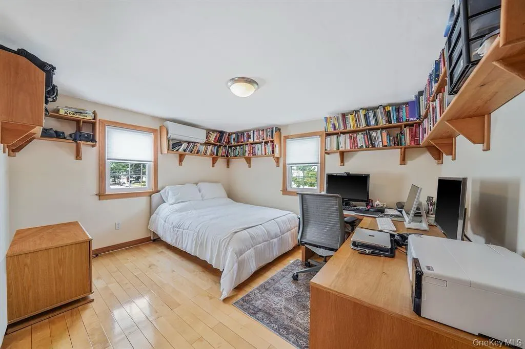 Bedroom with an office area, multiple windows, light wood-style flooring, and a wall unit AC Bedroom with an office area, multiple windows, light wood-style flooring, and a wall unit AC