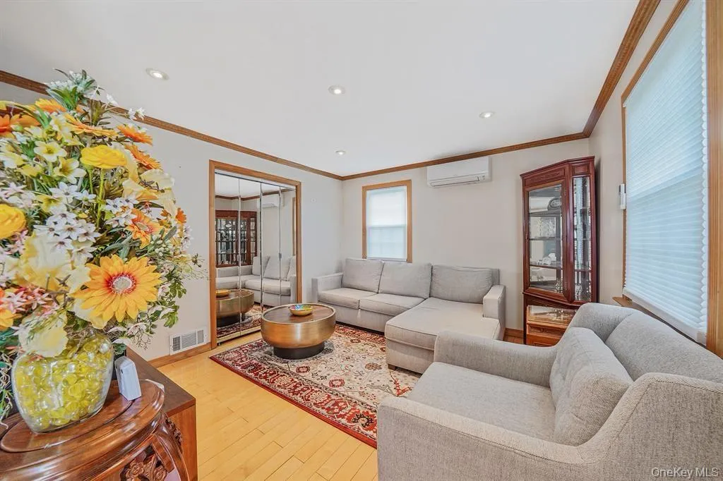 Living room with crown molding, light wood finished floors, an AC wall unit, and recessed lighting Living room with crown molding, light wood finished floors, an AC wall unit, and recessed lighting