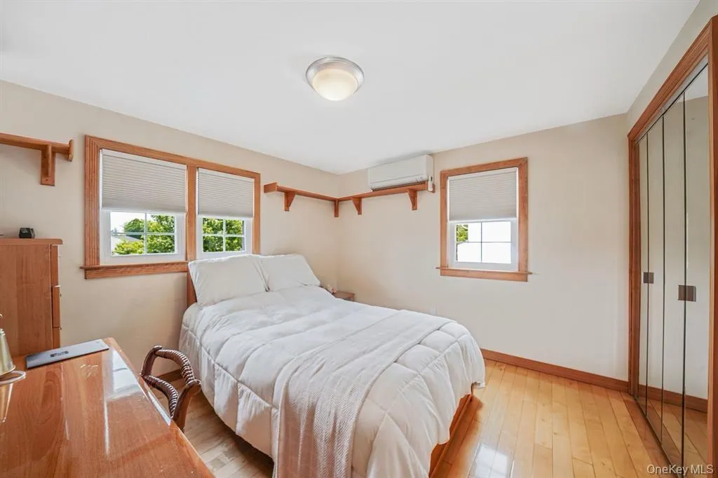 Bedroom featuring multiple windows, hardwood / wood-style floors, a wall mounted air conditioner, and a closet Bedroom featuring multiple windows, hardwood / wood-style floors, a wall mounted air conditioner, and a closet