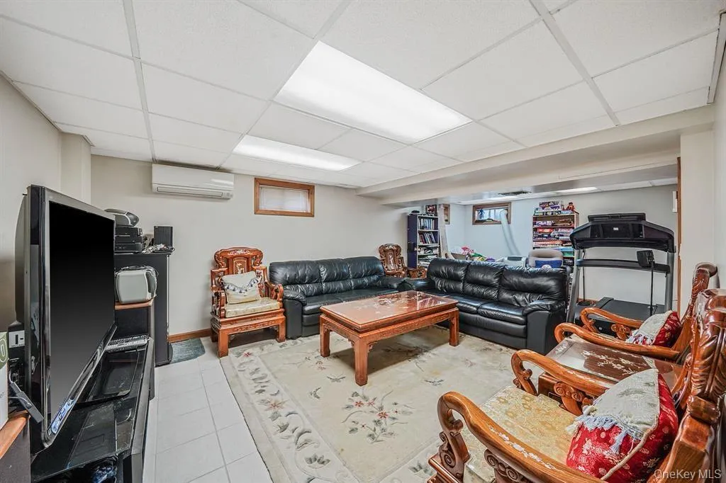 Living room with light tile patterned floors, a wall unit AC, and a drop ceiling Living room with light tile patterned floors, a wall unit AC, and a drop ceiling