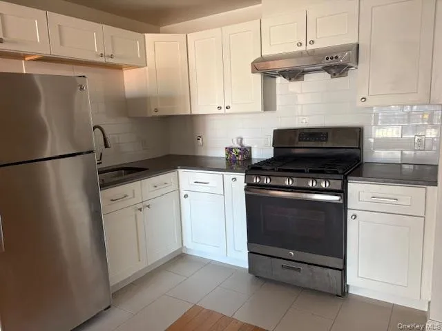 Kitchen featuring appliances with stainless steel finishes, decorative backsplash, white cabinets, and under cabinet range hood Kitchen featuring appliances with stainless steel finishes, decorative backsplash, white cabinets, and under cabinet range hood