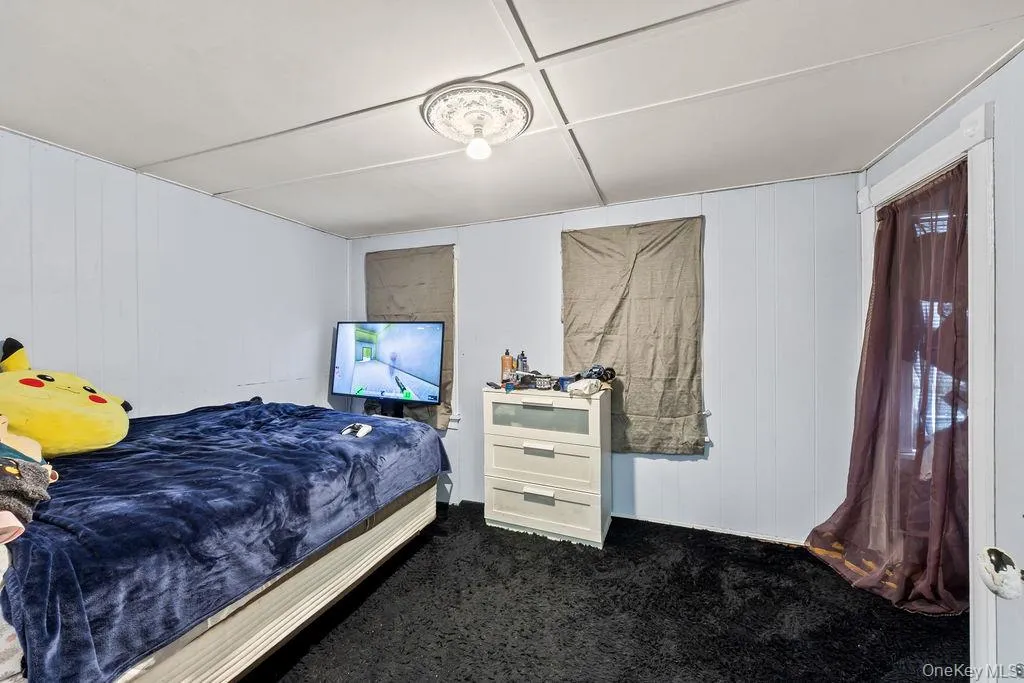 Carpeted bedroom featuring wooden walls and a decorative wall Carpeted bedroom featuring wooden walls and a decorative wall