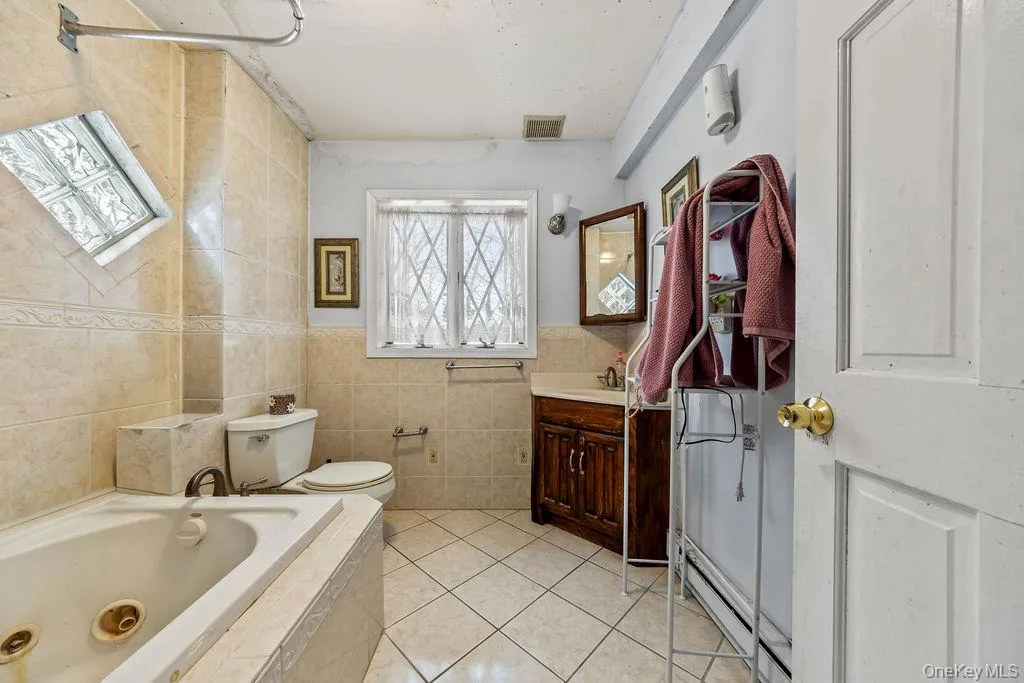 Full bathroom with light tile patterned floors, a baseboard heating unit, vanity, tile walls, and a whirlpool tub Full bathroom with light tile patterned floors, a baseboard heating unit, vanity, tile walls, and a whirlpool tub