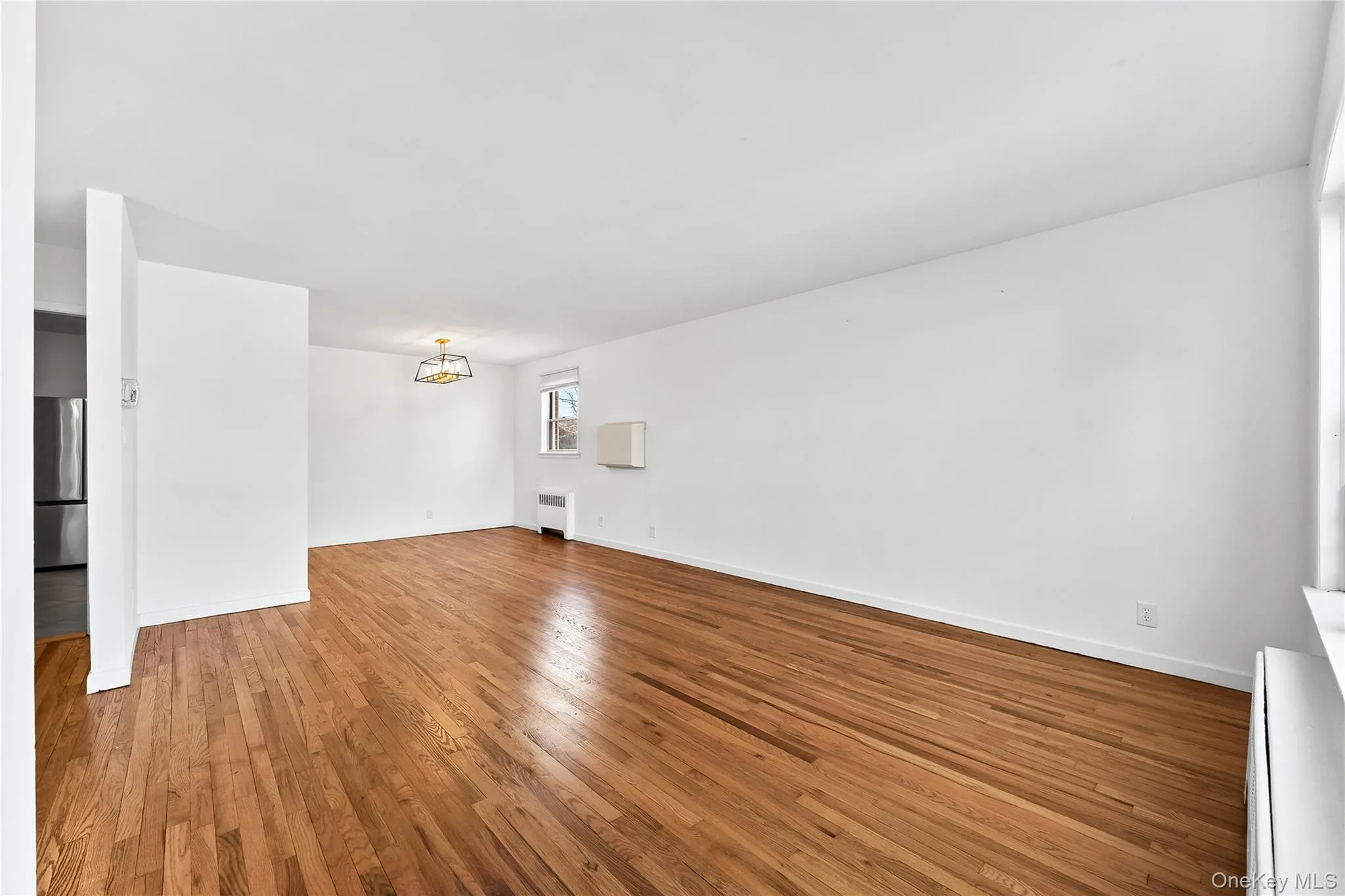 Unfurnished living room with a chandelier, light wood-style floors, baseboard heating, and radiator heating unit Unfurnished living room with a chandelier, light wood-style floors, baseboard heating, and radiator heating unit