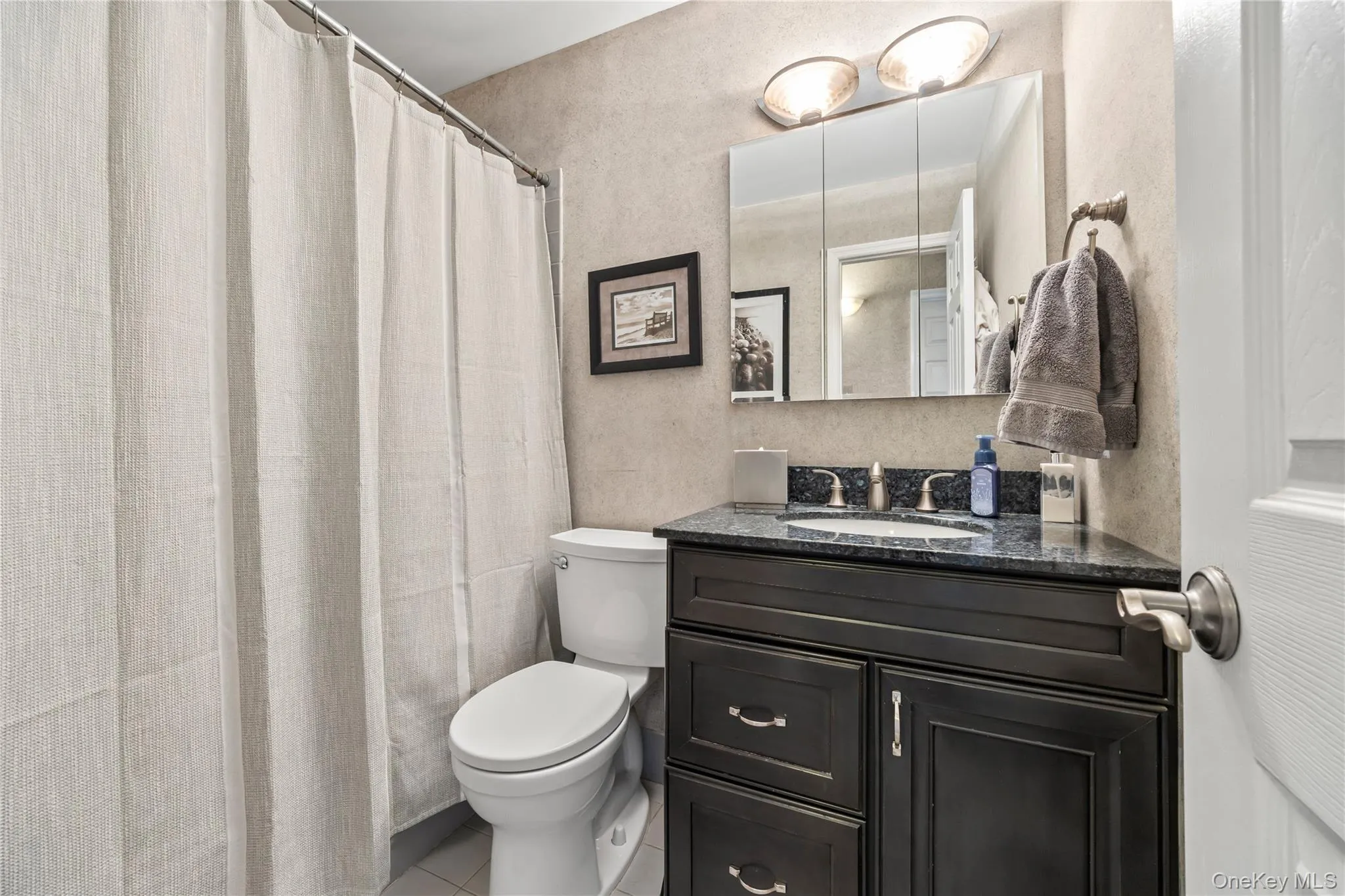 Bathroom featuring a textured wall, a shower with curtain, vanity, and light tile patterned flooring Bathroom featuring a textured wall, a shower with curtain, vanity, and light tile patterned flooring