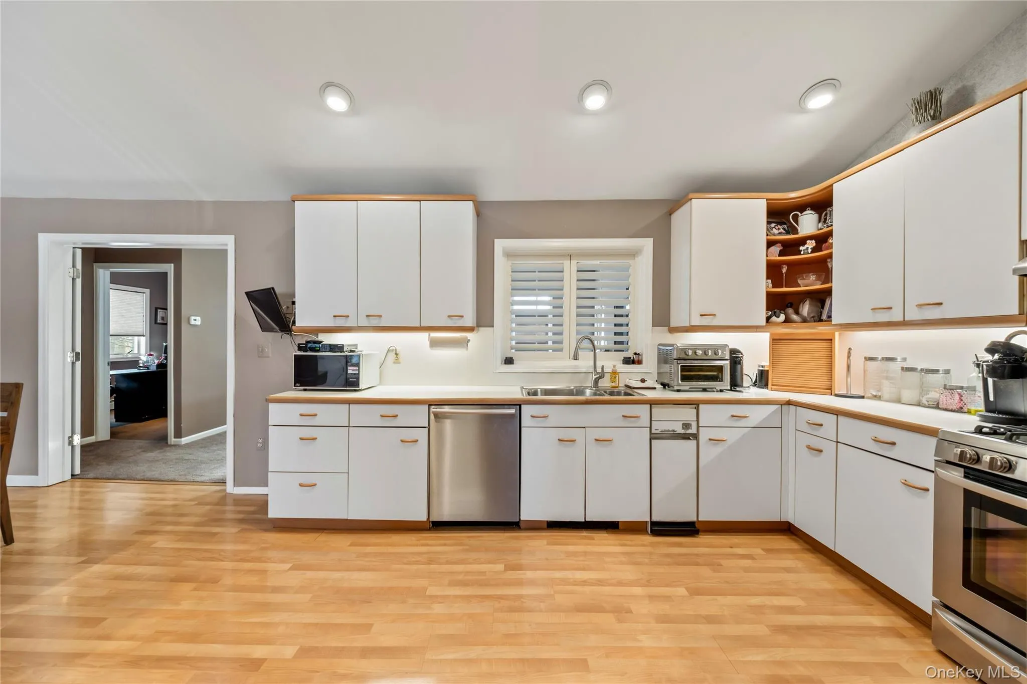 Kitchen featuring open shelves, white cabinetry, light countertops, stainless steel appliances, and light wood-type flooring Kitchen featuring open shelves, white cabinetry, light countertops, stainless steel appliances, and light wood-type flooring