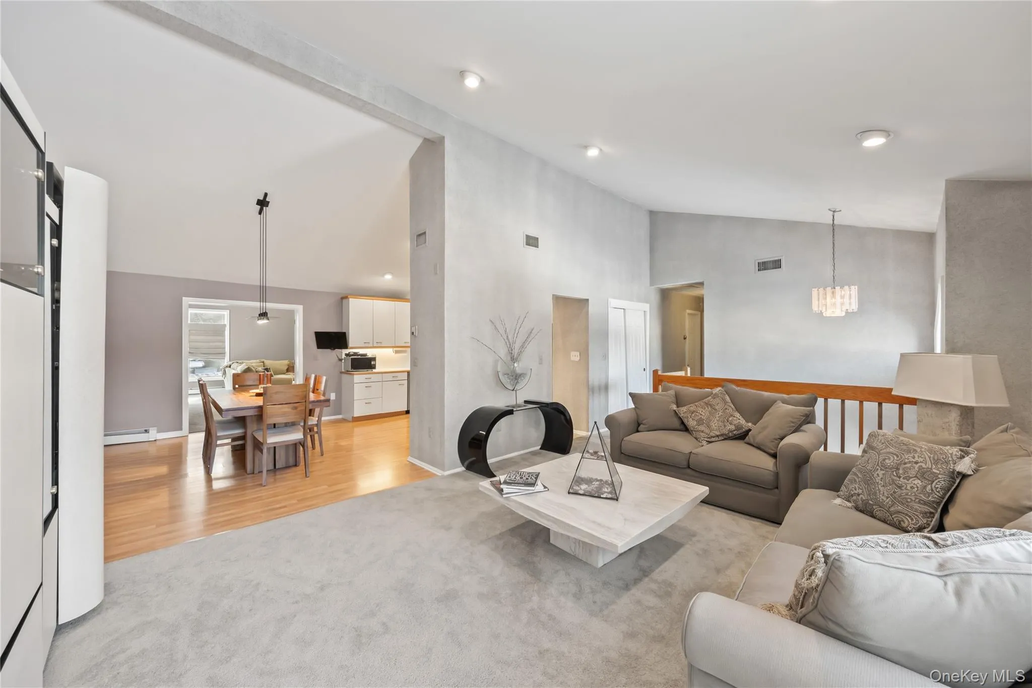 Living room with light carpet, high vaulted ceiling, baseboard heating, and light wood-style floors Living room with light carpet, high vaulted ceiling, baseboard heating, and light wood-style floors