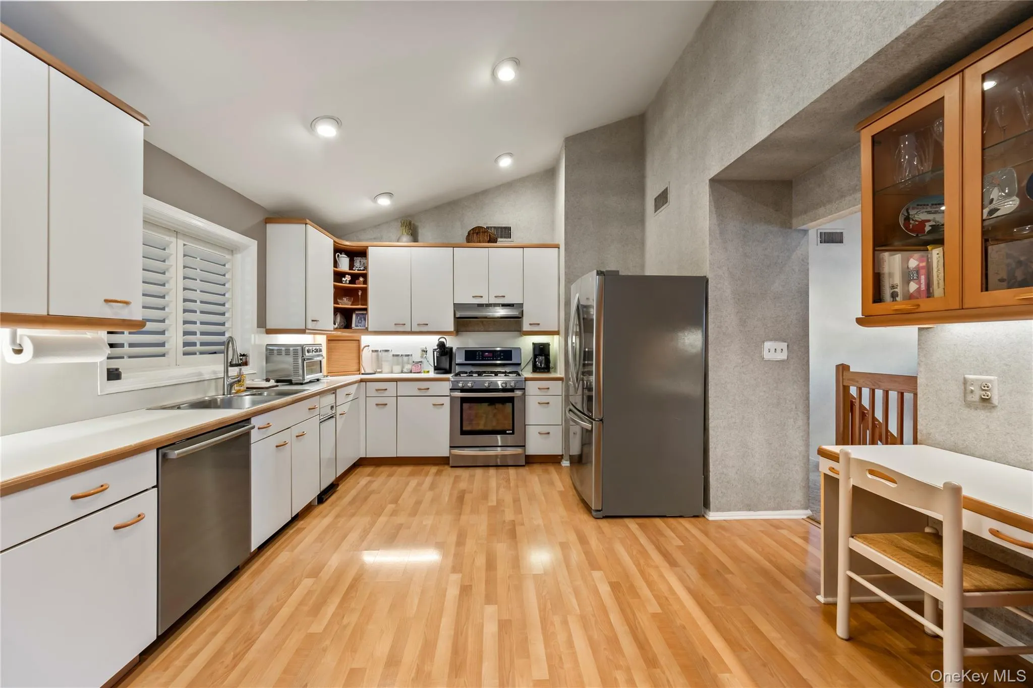 Kitchen featuring open shelves, light countertops, appliances with stainless steel finishes, white cabinets, and light wood finished floors Kitchen featuring open shelves, light countertops, appliances with stainless steel finishes, white cabinets, and light wood finished floors