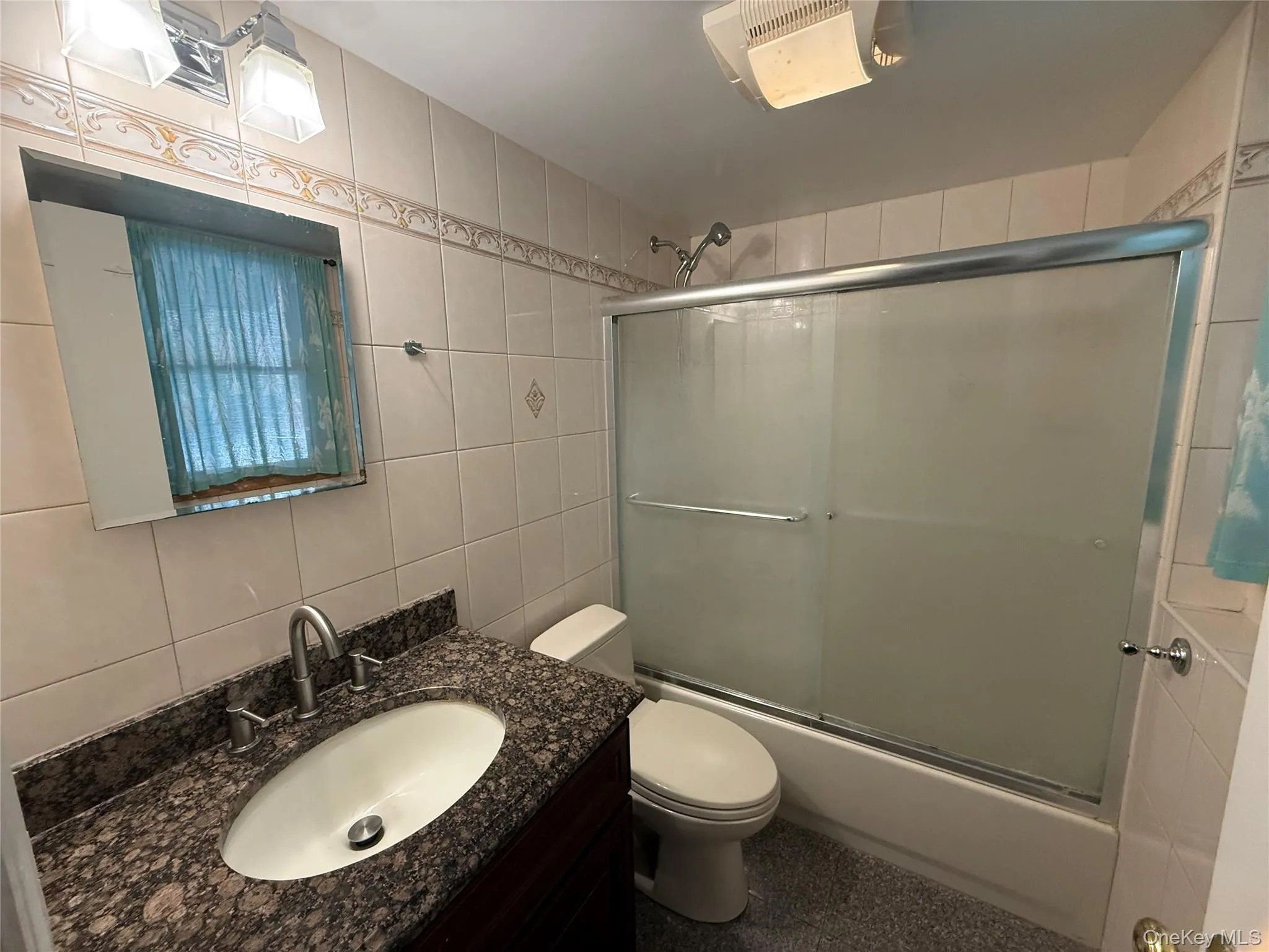 Full bathroom featuring tile walls, vanity, combined bath / shower with glass door, and tasteful backsplash Full bathroom featuring tile walls, vanity, combined bath / shower with glass door, and tasteful backsplash