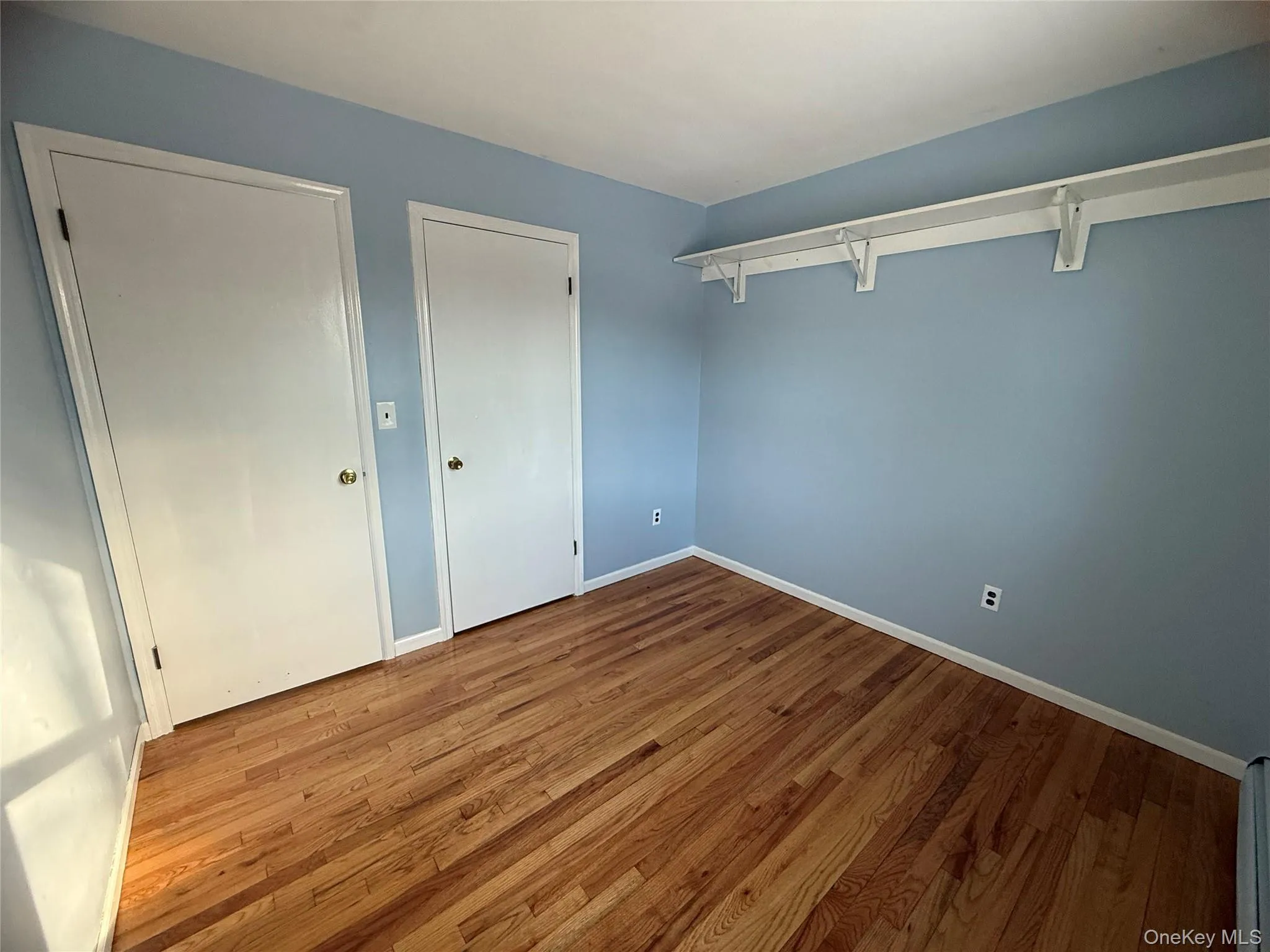 Unfurnished bedroom with wood finished floors and baseboard heating Unfurnished bedroom with wood finished floors and baseboard heating