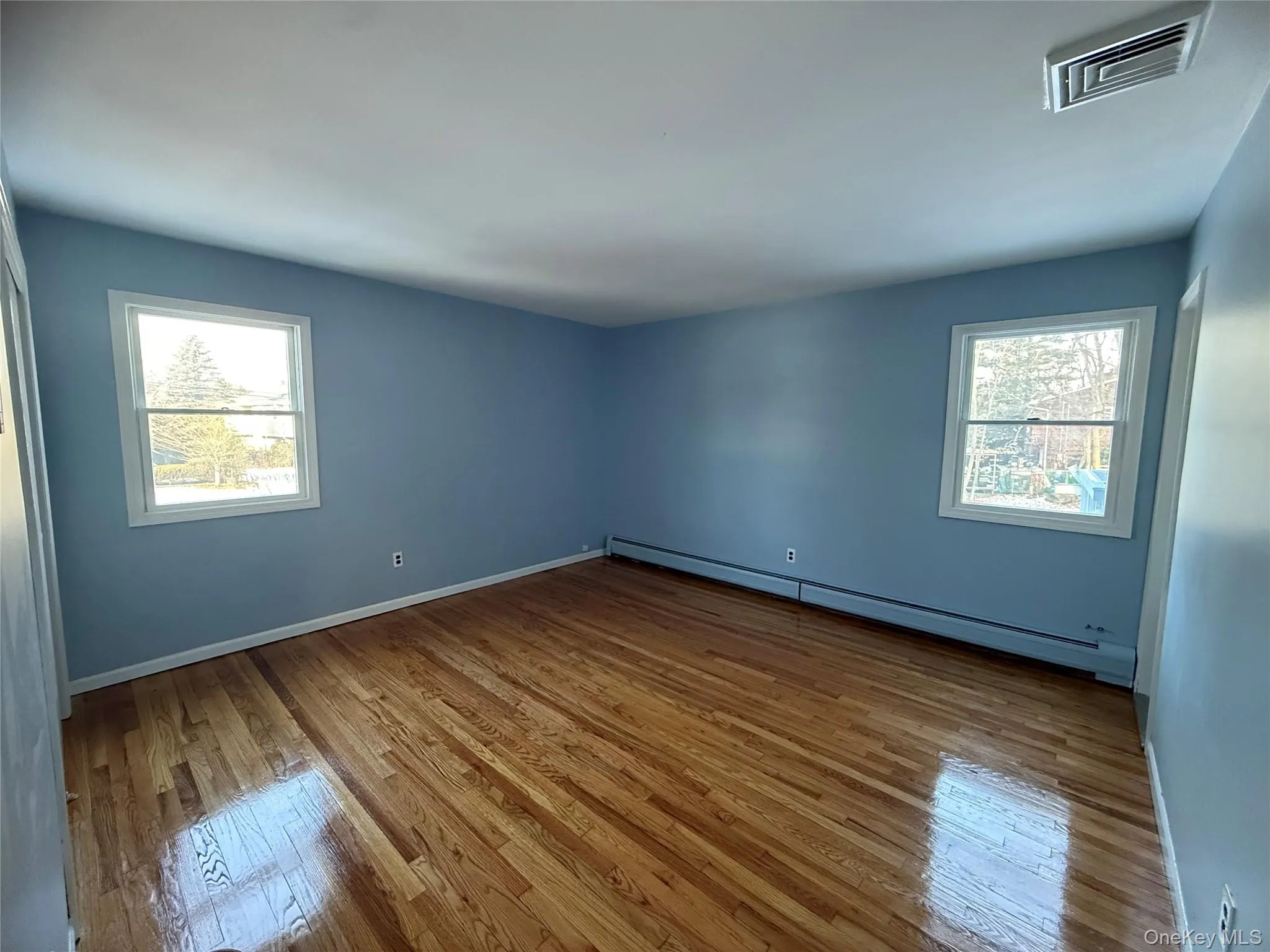 Unfurnished room with a baseboard radiator, hardwood / wood-style floors, and plenty of natural light Unfurnished room with a baseboard radiator, hardwood / wood-style floors, and plenty of natural light