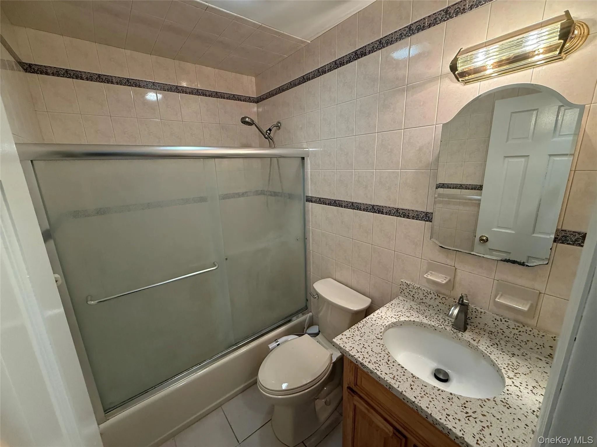 Bathroom featuring vanity, tile walls, shower / bath combination with glass door, and tile patterned flooring Bathroom featuring vanity, tile walls, shower / bath combination with glass door, and tile patterned flooring