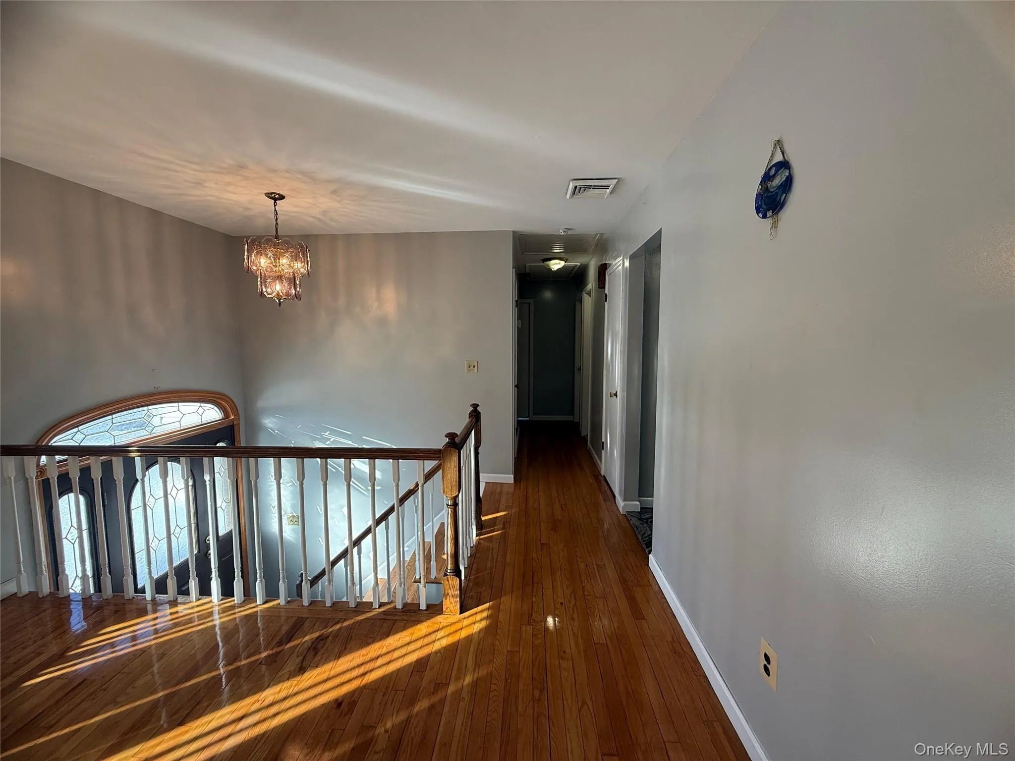 Hallway with an upstairs landing, a chandelier, and dark wood-type flooring Hallway with an upstairs landing, a chandelier, and dark wood-type flooring