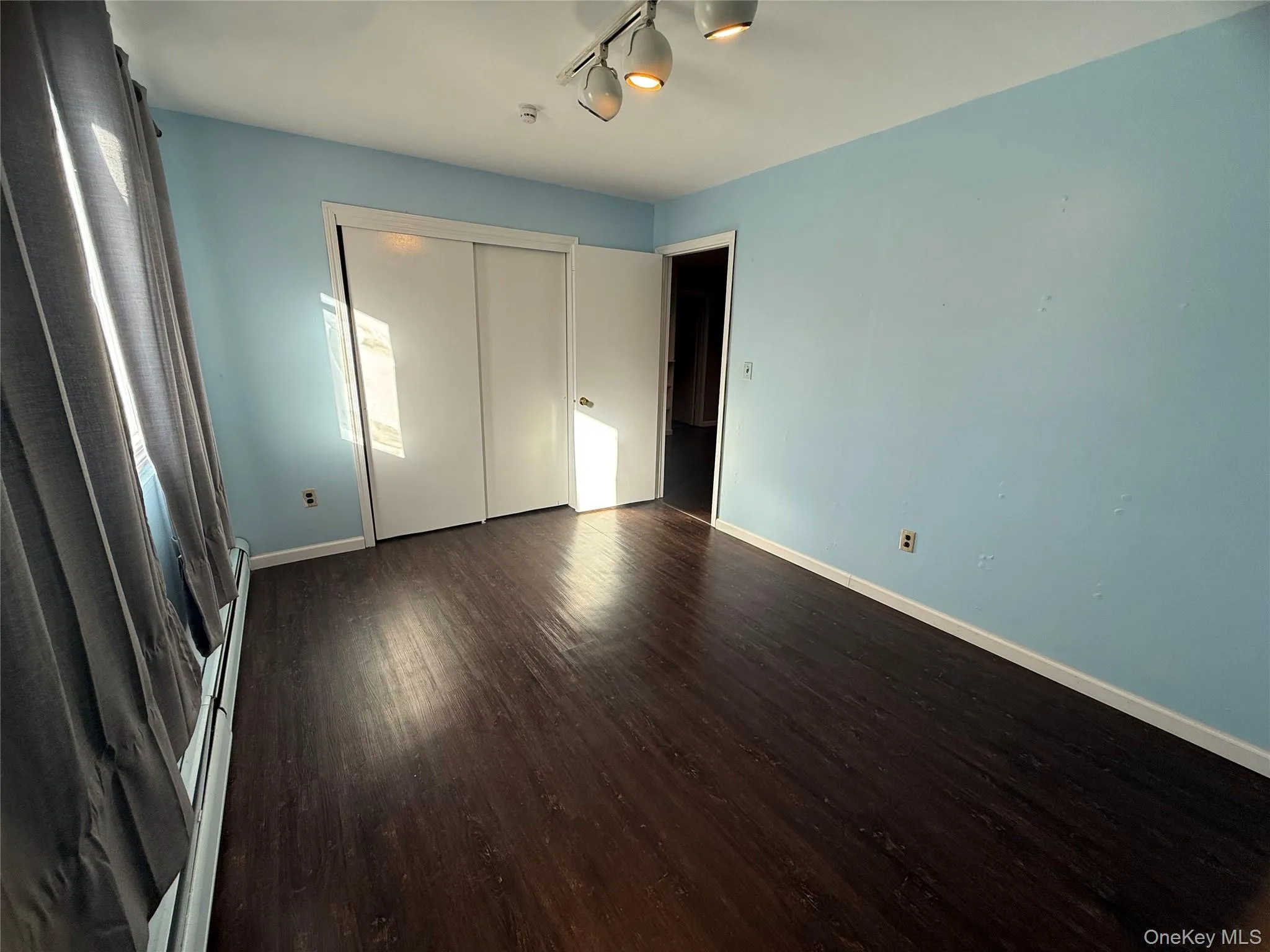 Unfurnished bedroom featuring dark wood-type flooring, baseboard heating, and a closet Unfurnished bedroom featuring dark wood-type flooring, baseboard heating, and a closet