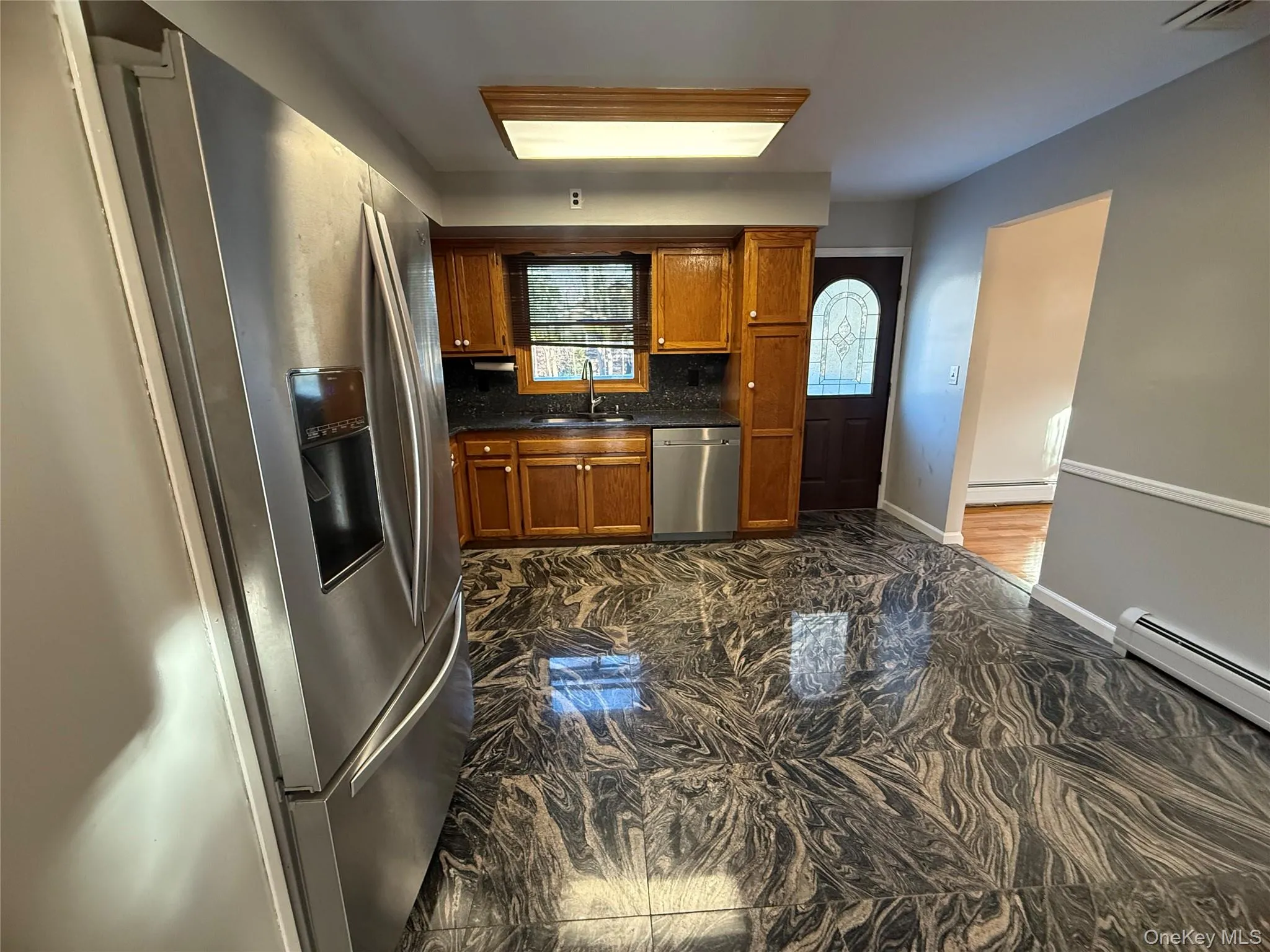 Kitchen with stainless steel appliances, brown cabinetry, a baseboard heating unit, and backsplash Kitchen with stainless steel appliances, brown cabinetry, a baseboard heating unit, and backsplash