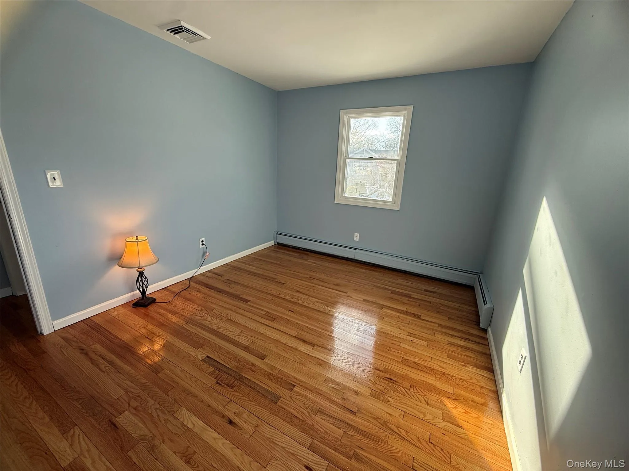 Spare room featuring wood finished floors and a baseboard heating unit Spare room featuring wood finished floors and a baseboard heating unit