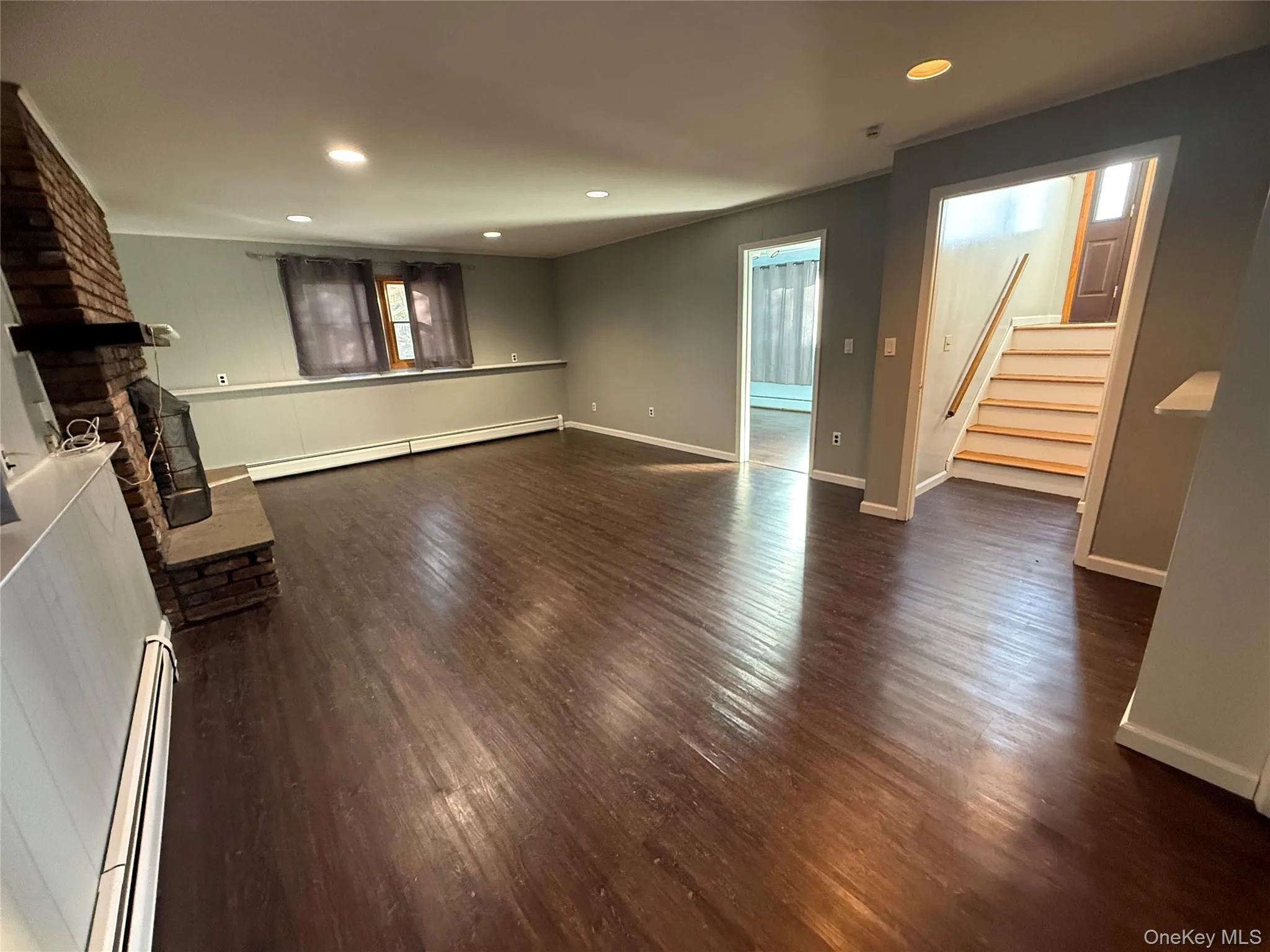 Unfurnished living room featuring stairway, recessed lighting, baseboard heating, and dark wood-type flooring Unfurnished living room featuring stairway, recessed lighting, baseboard heating, and dark wood-type flooring