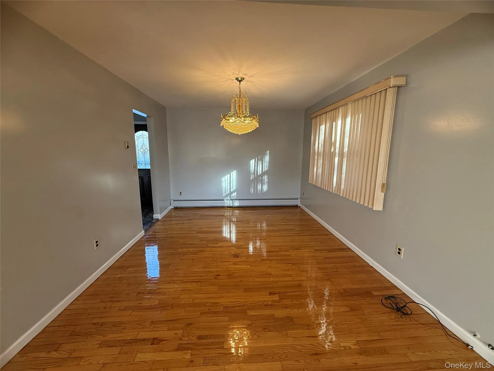 Unfurnished dining area with light wood-type flooring, a chandelier, and a baseboard radiator Unfurnished dining area with light wood-type flooring, a chandelier, and a baseboard radiator
