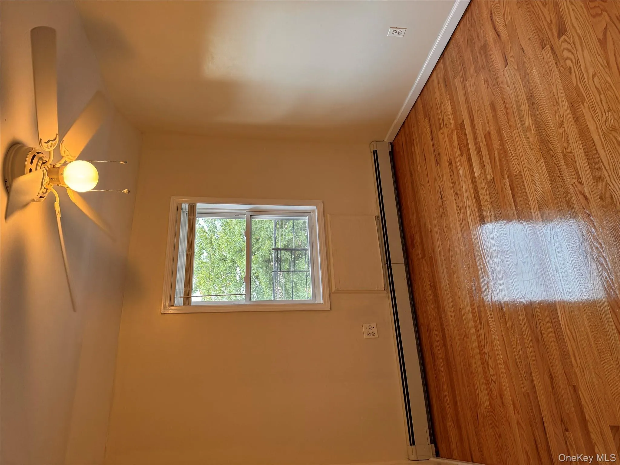 Empty room with baseboard heating, ceiling fan, and light wood finished floors Empty room with baseboard heating, ceiling fan, and light wood finished floors