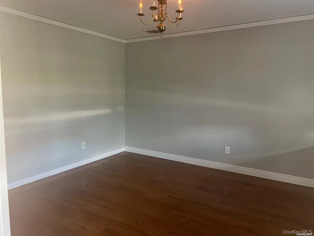 Spare room featuring a chandelier, ornamental molding, and dark wood finished floors Spare room featuring a chandelier, ornamental molding, and dark wood finished floors