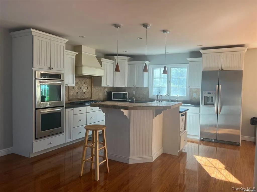 Kitchen featuring stainless steel appliances, a kitchen breakfast bar, white cabinets, and decorative light fixtures Kitchen featuring stainless steel appliances, a kitchen breakfast bar, white cabinets, and decorative light fixtures