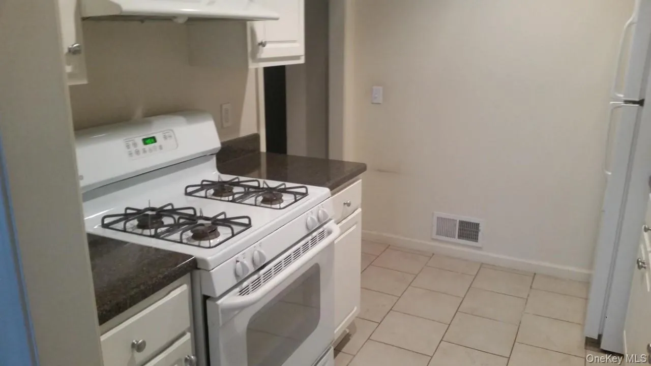 Kitchen featuring white appliances, white cabinetry, under cabinet range hood, light tile patterned floors, and dark stone countertops Kitchen featuring white appliances, white cabinetry, under cabinet range hood, light tile patterned floors, and dark stone countertops